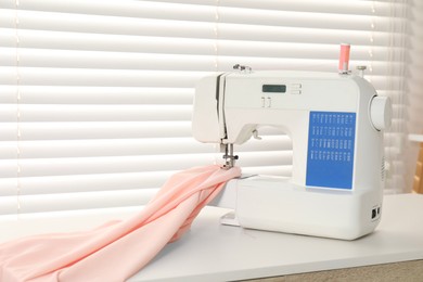 Photo of Sewing machine and fabric on white table indoors