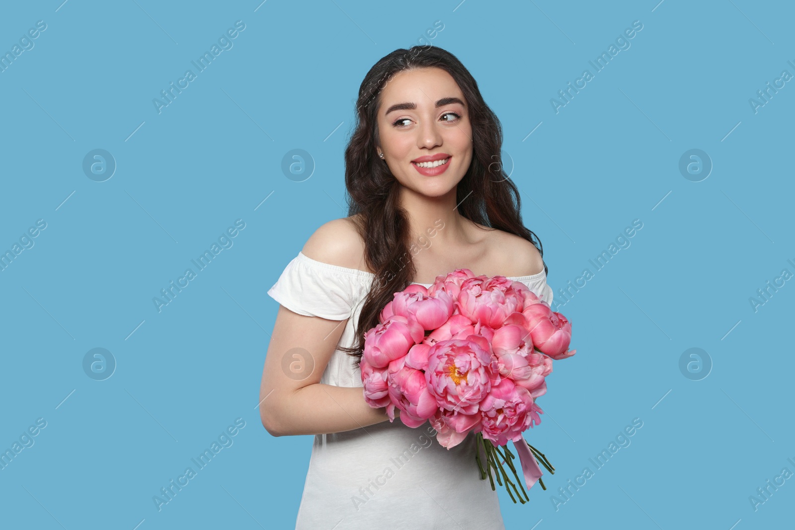 Photo of Beautiful young woman with bouquet of pink peonies on light blue background