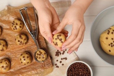 Woman making delicious chocolate chip cookies at white wooden table, top view