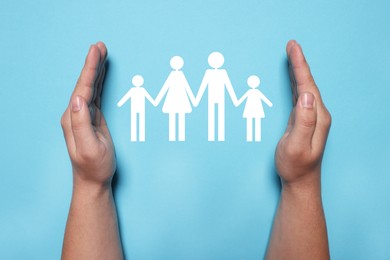 Image of Man holding hands around paper silhouette of family on light blue background, top view. Insurance concept