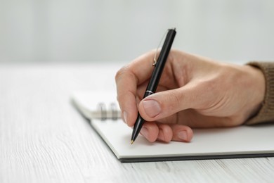 Man writing in notebook at white wooden table, closeup. Space for text