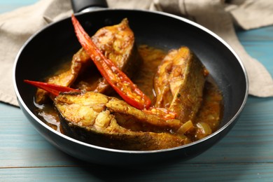 Photo of Tasty fish curry in frying pan on light blue wooden table, closeup. Indian cuisine