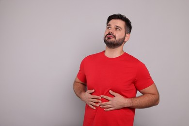 Man suffering from stomach pain on grey background, space for text