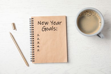Image of Notebook with inscription New Year Goals, cup of coffee and pen on white wooden table, flat lay