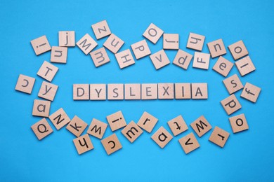 Photo of Wooden cubes with word Dyslexia on light blue background, flat lay