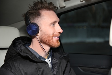 Photo of Young man listening to music with headphones in car. Space for text