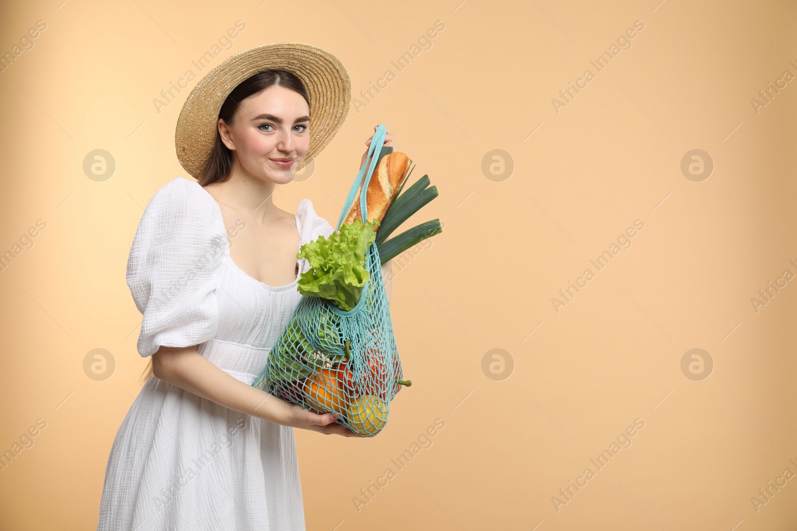 Photo of Woman with string bag of fresh vegetables and baguette on beige background, space for text