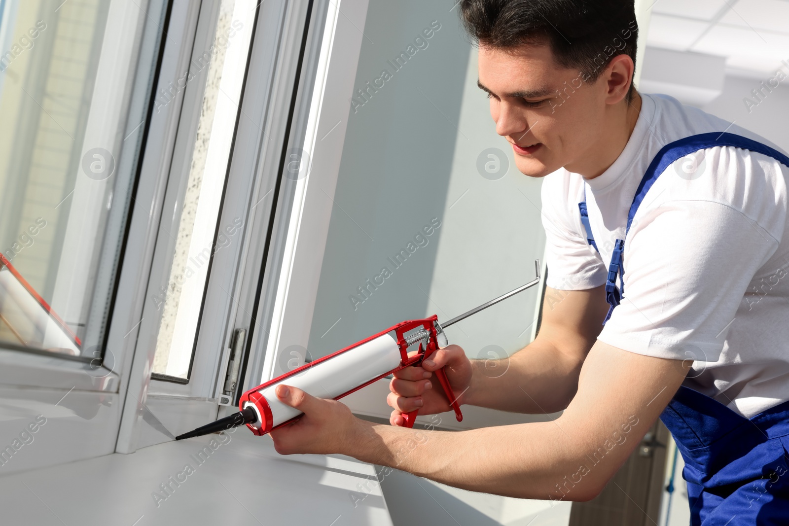 Photo of Worker sealing plastic window with caulk indoors. Installation process