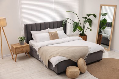 Photo of Stylish bedroom interior with large bed, mirror and houseplants