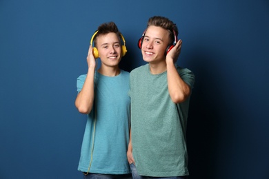 Teenage twin brothers with headphones on color background