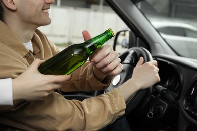 Photo of Smiling man taking bottle of beer while driving car, closeup. Don't drink and drive concept