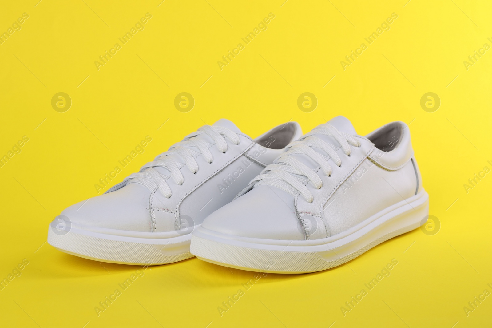 Photo of Pair of stylish white sneakers on yellow background