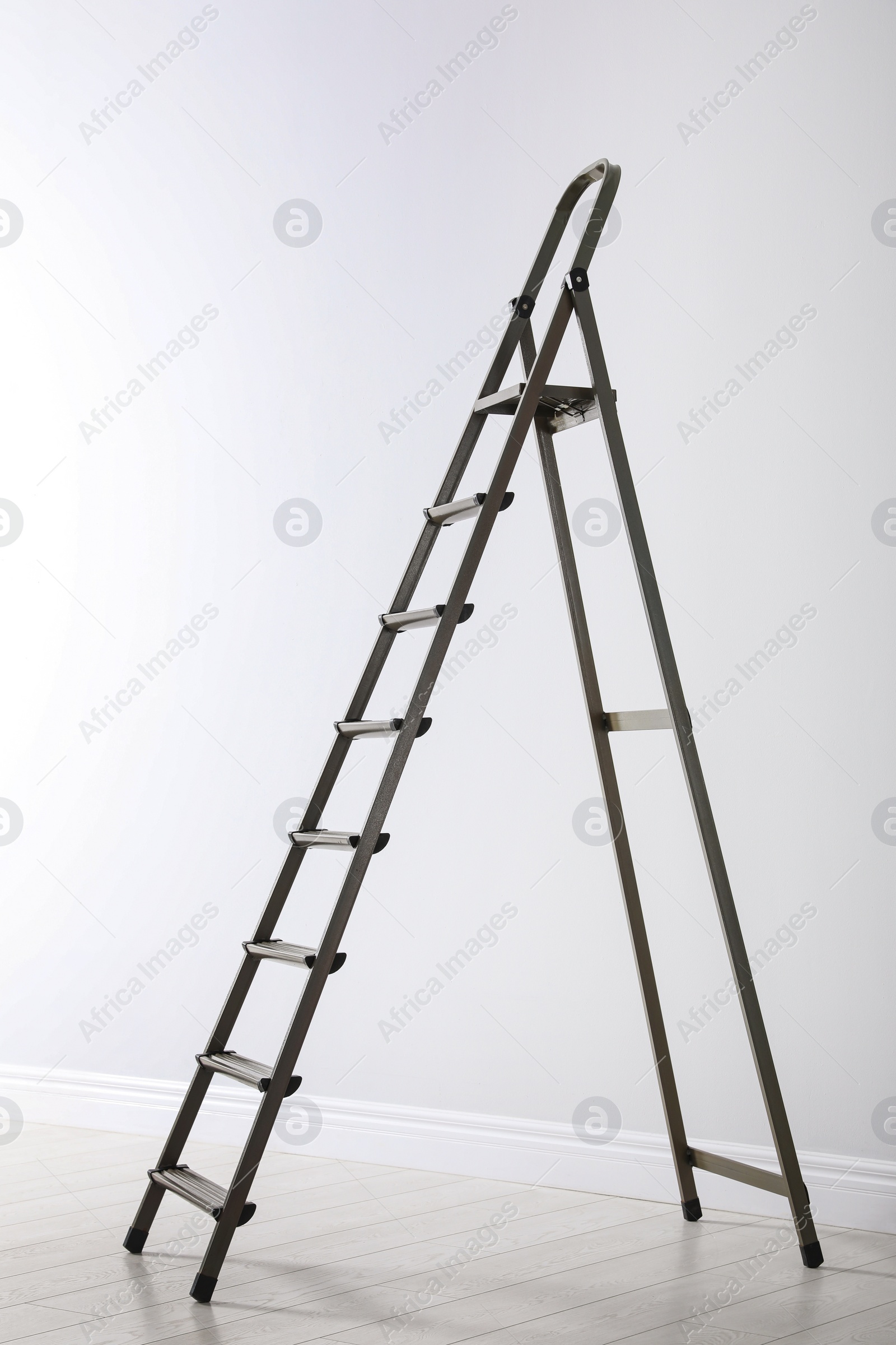 Photo of Modern metal stepladder near white wall indoors