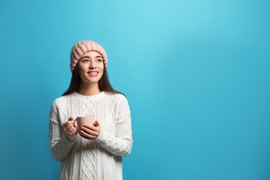 Young woman in sweater with cup of hot coffee on color background, space for text. Winter season