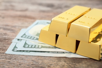 Photo of Gold bars and dollar bills on wooden table, closeup. Space for text