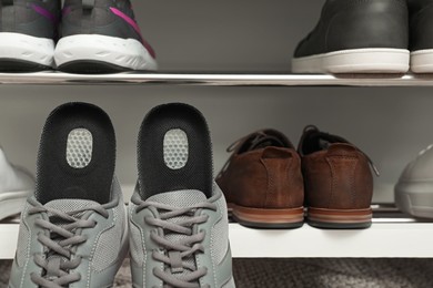 Photo of Orthopedic insoles in shoes near rack, closeup