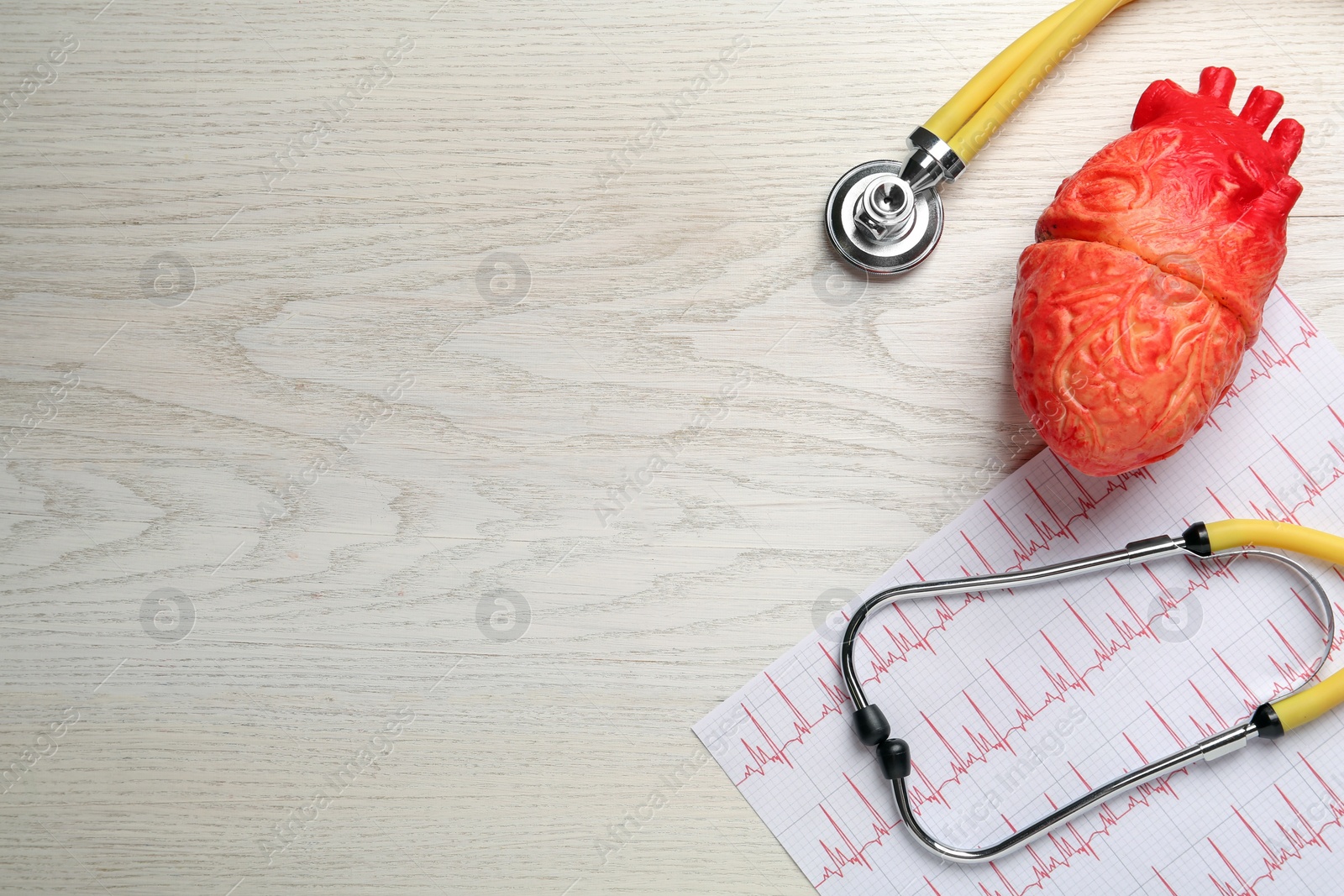 Photo of Stethoscope, red heart model and cardiogram on white wooden table, flat lay with space for text. Cardiology concept