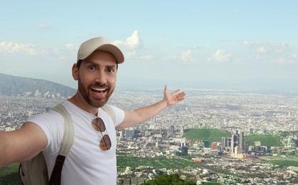 Image of Smiling man taking selfie against valley with city in mountains