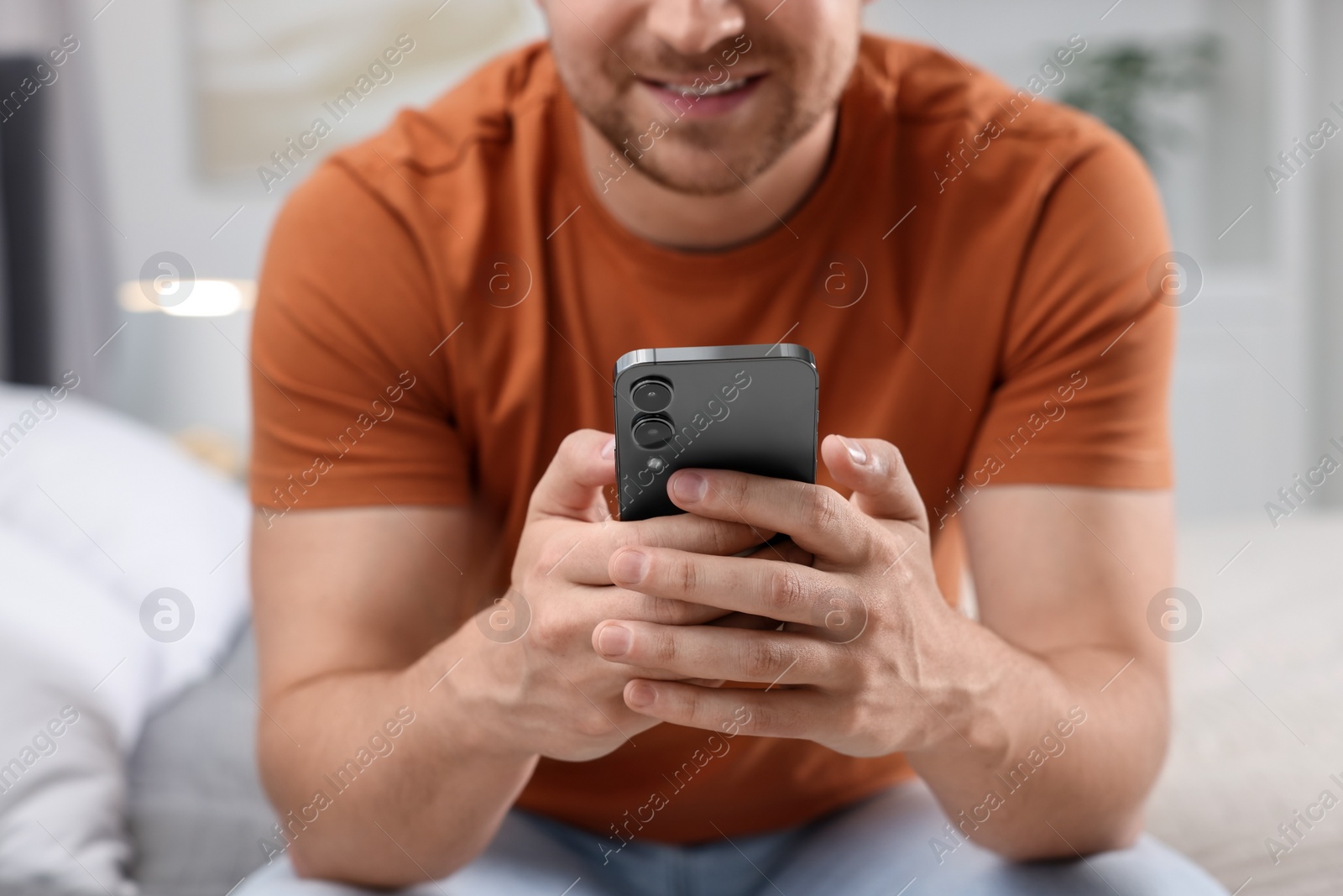 Photo of Man sending message via smartphone on bed at home, closeup