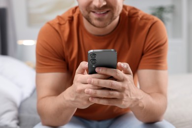 Photo of Man sending message via smartphone on bed at home, closeup