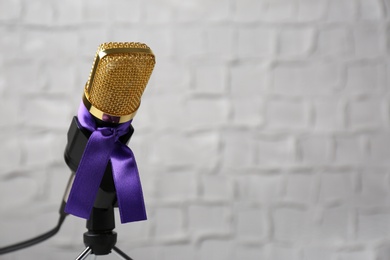 Photo of Microphone with purple awareness ribbon against white wall, space for text