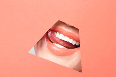 Photo of Lips of young woman with beautiful lipstick visible through hole in color paper