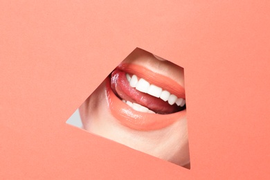 Lips of young woman with beautiful lipstick visible through hole in color paper