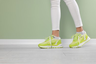 Photo of Woman wearing new stylish sneakers near light green wall, closeup. Space for text