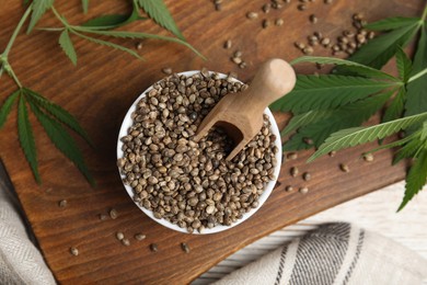 Photo of Organic hemp seeds and leaves on wooden board, flat lay