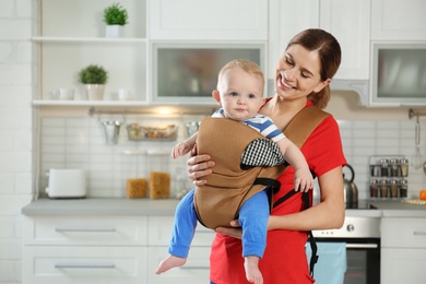 Woman with her son in baby carrier at home. Space for text