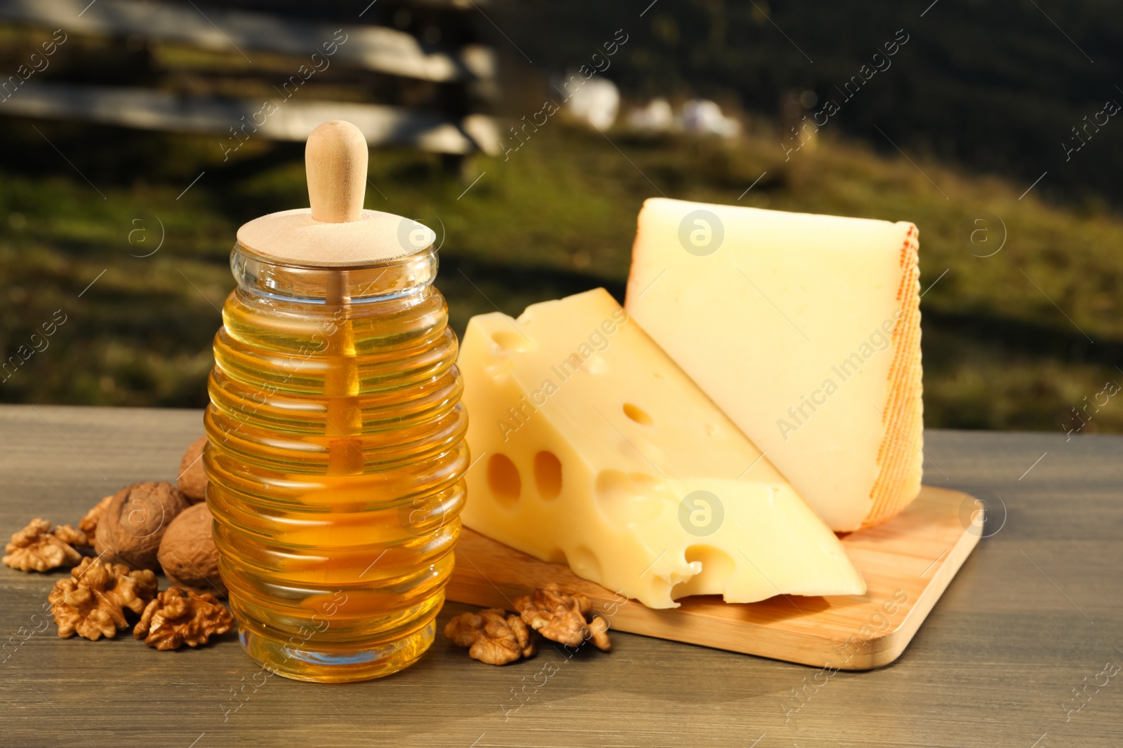 Photo of Fresh aromatic honey, cheese and nuts on wooden table outdoors