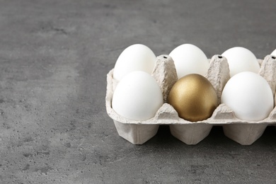 Photo of Carton with golden egg and others on grey background, space for text