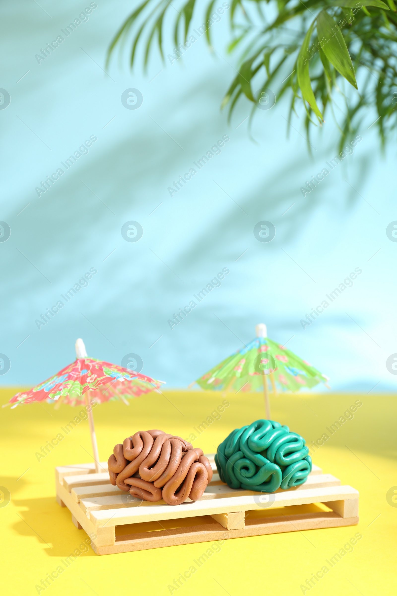 Photo of Brains made of plasticine on mini wooden sunbed under umbrellas against color background, space for text