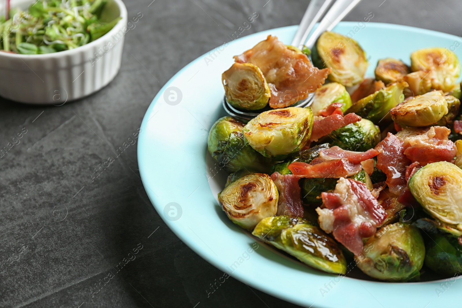 Photo of Delicious roasted Brussels sprouts with bacon served on black table, closeup