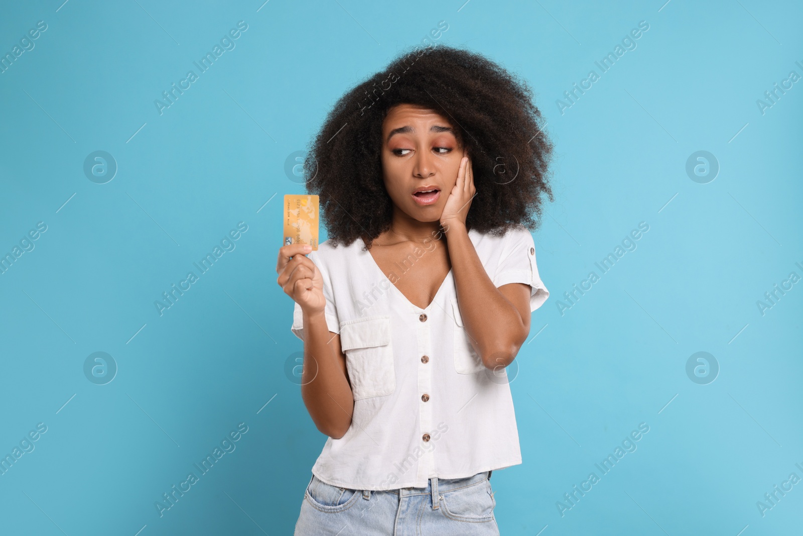 Photo of Confused woman with credit card on light blue background. Debt problem