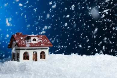 Photo of Decorative house in snowdrift on color background, space for text. Winter weather