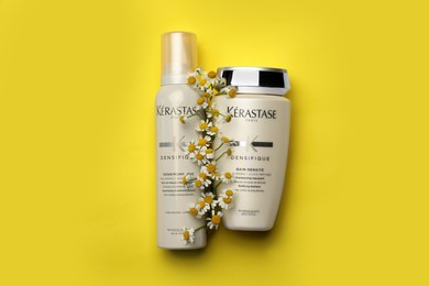 Photo of MYKOLAIV, UKRAINE - SEPTEMBER 07, 2021: Kerastase hair care cosmetic products and chamomiles on yellow background, flat lay