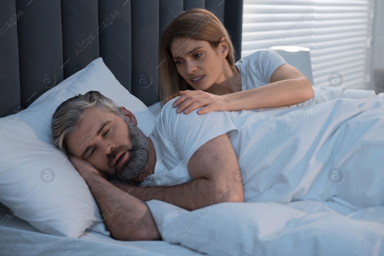 Photo of Irritated woman waking up her snoring husband in bed at home