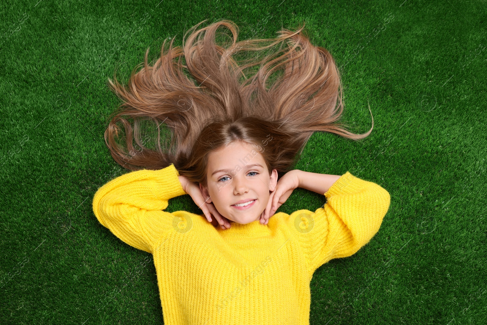 Photo of Little smiling girl on green grass, top view