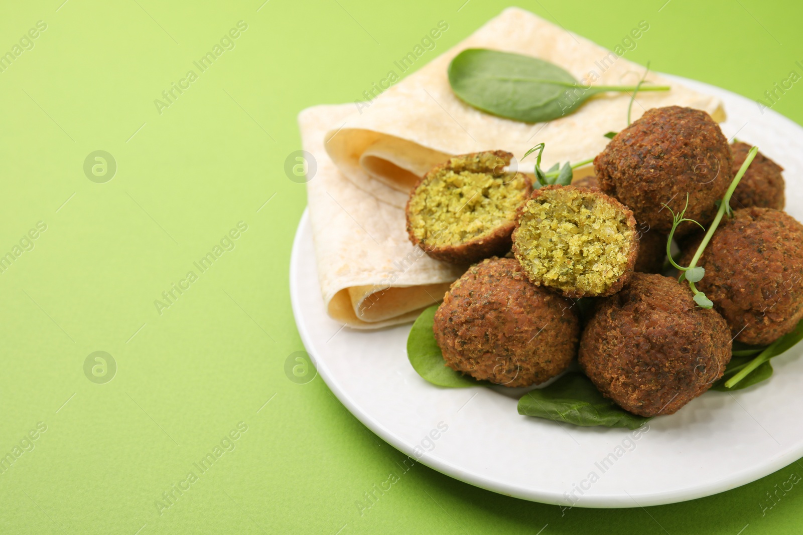 Photo of Delicious falafel balls, herbs and lavash on green background, space for text