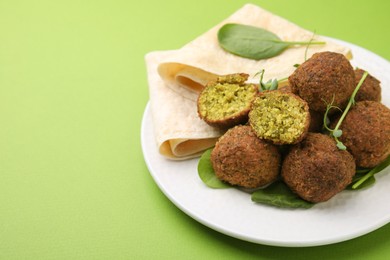 Photo of Delicious falafel balls, herbs and lavash on green background, space for text