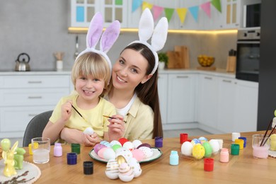 Mother and her cute son painting Easter eggs at table in kitchen