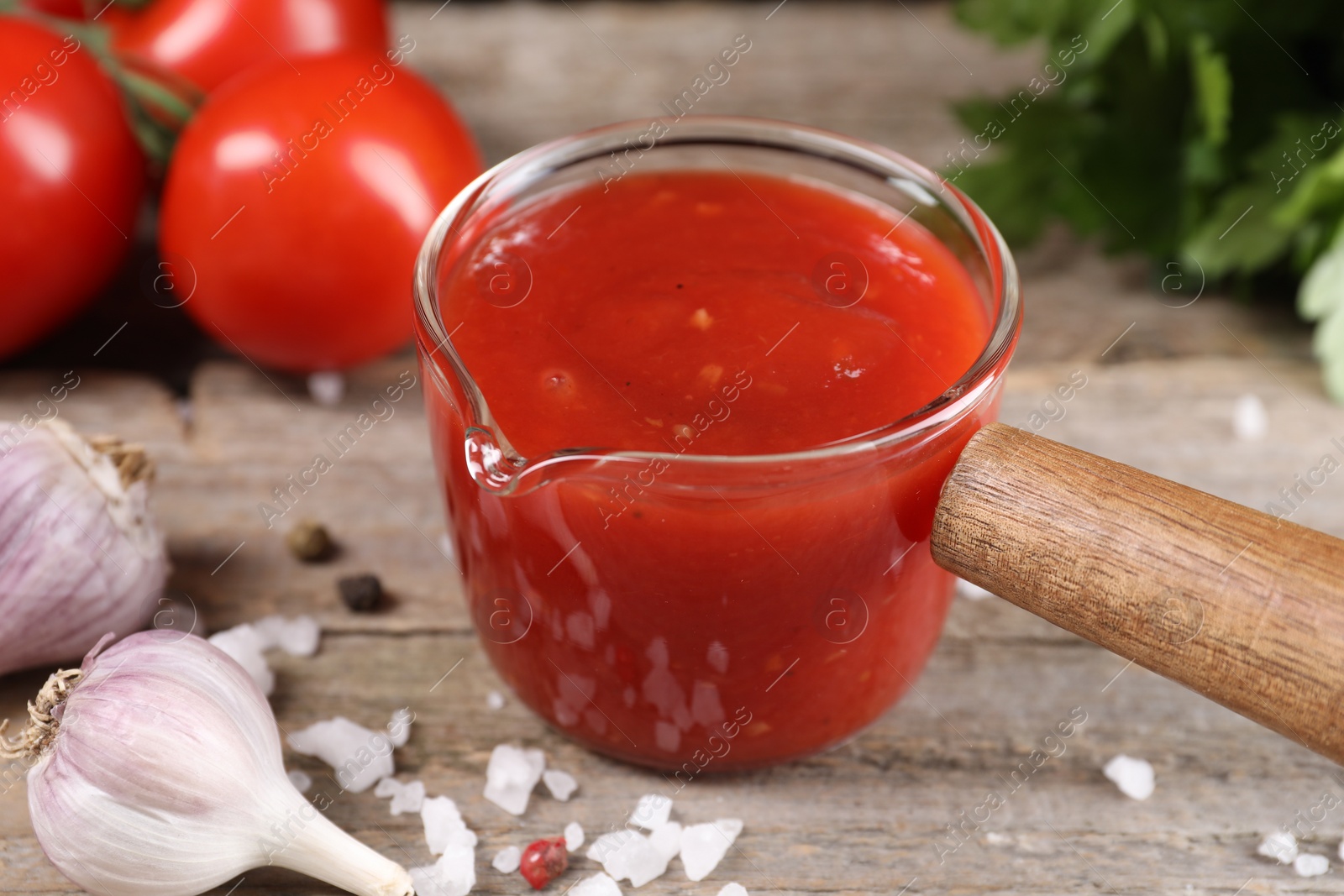 Photo of Delicious ketchup, salt and garlic on wooden table, closeup. Tomato sauce