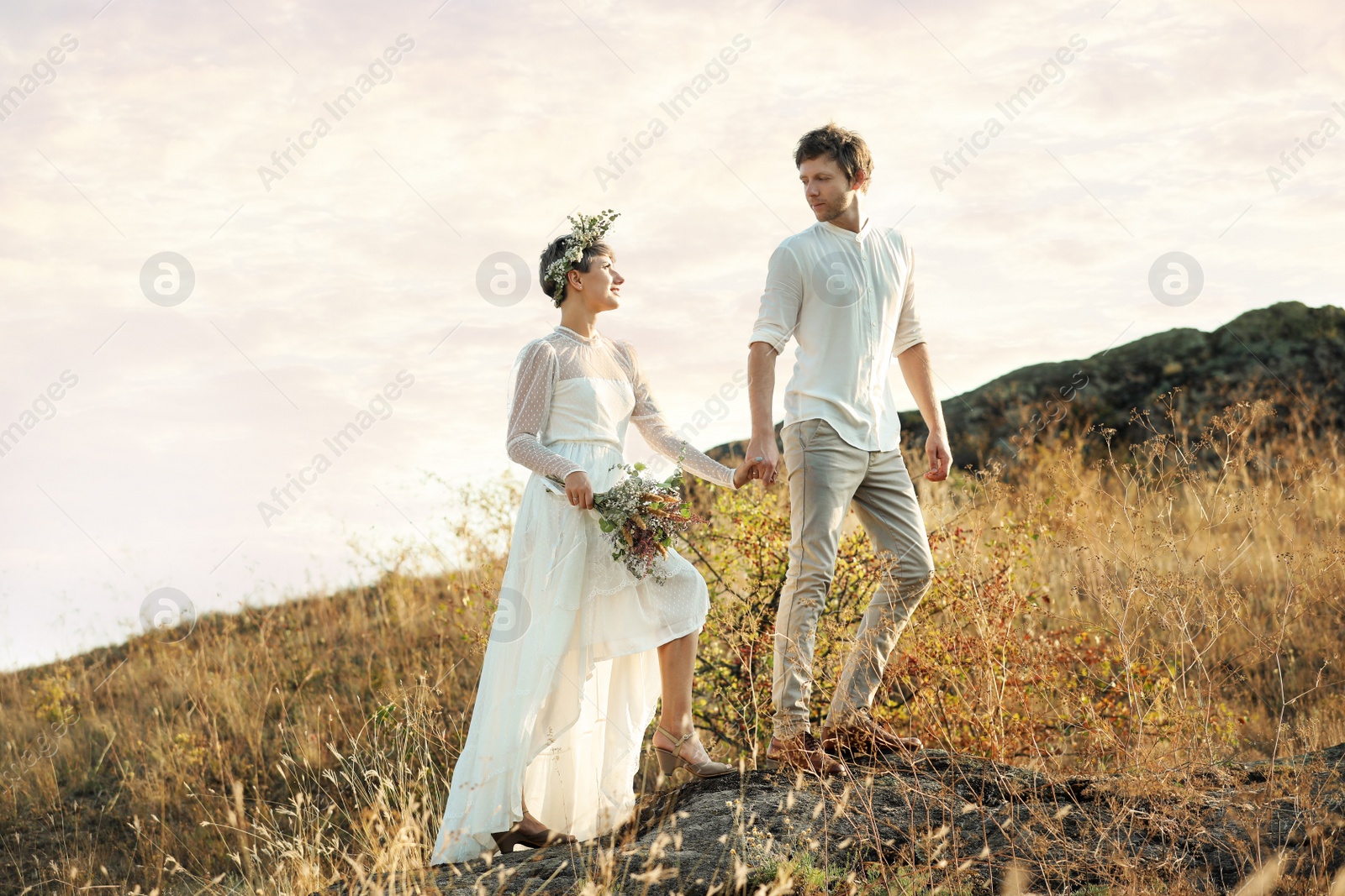 Photo of Happy newlyweds with beautiful field bouquet outdoors