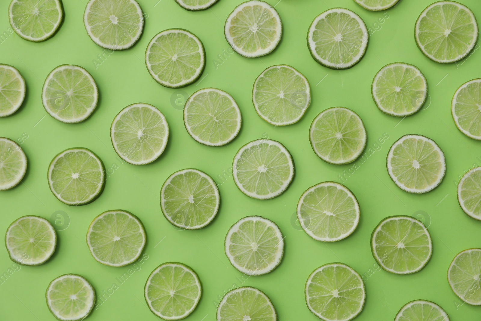 Photo of Slices of fresh juicy limes on green background, flat lay