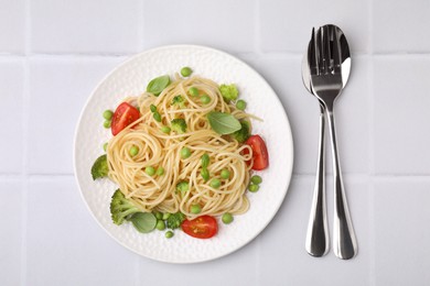 Plate of delicious pasta primavera and cutlery on white tiled table, flat lay