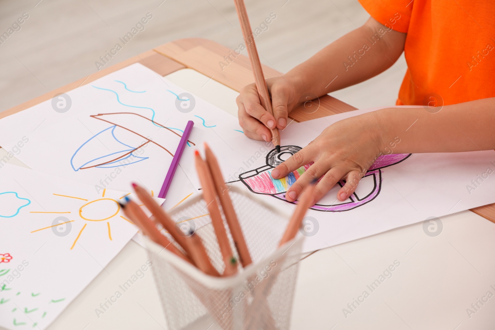 Photo of Little child drawing picture on paper at desk, closeup. Kindergarten activity