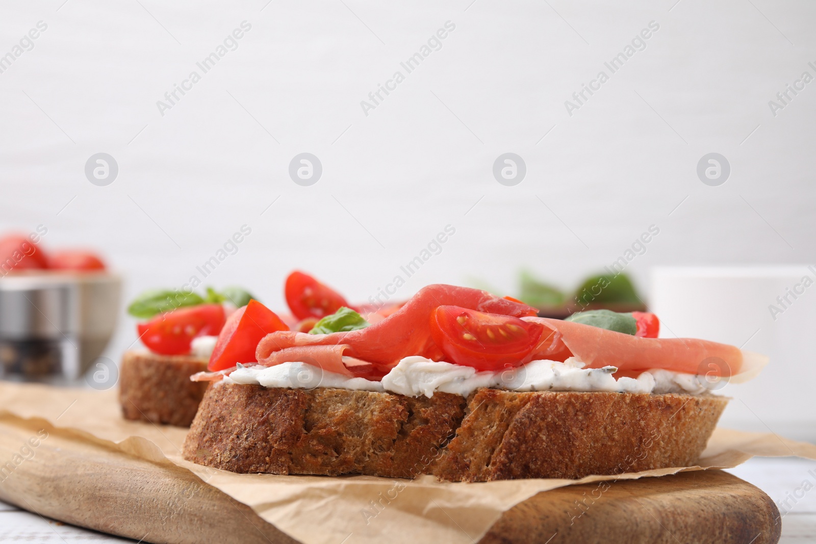 Photo of Tasty bruschettas with prosciutto, tomatoes and cheese on wooden board, closeup