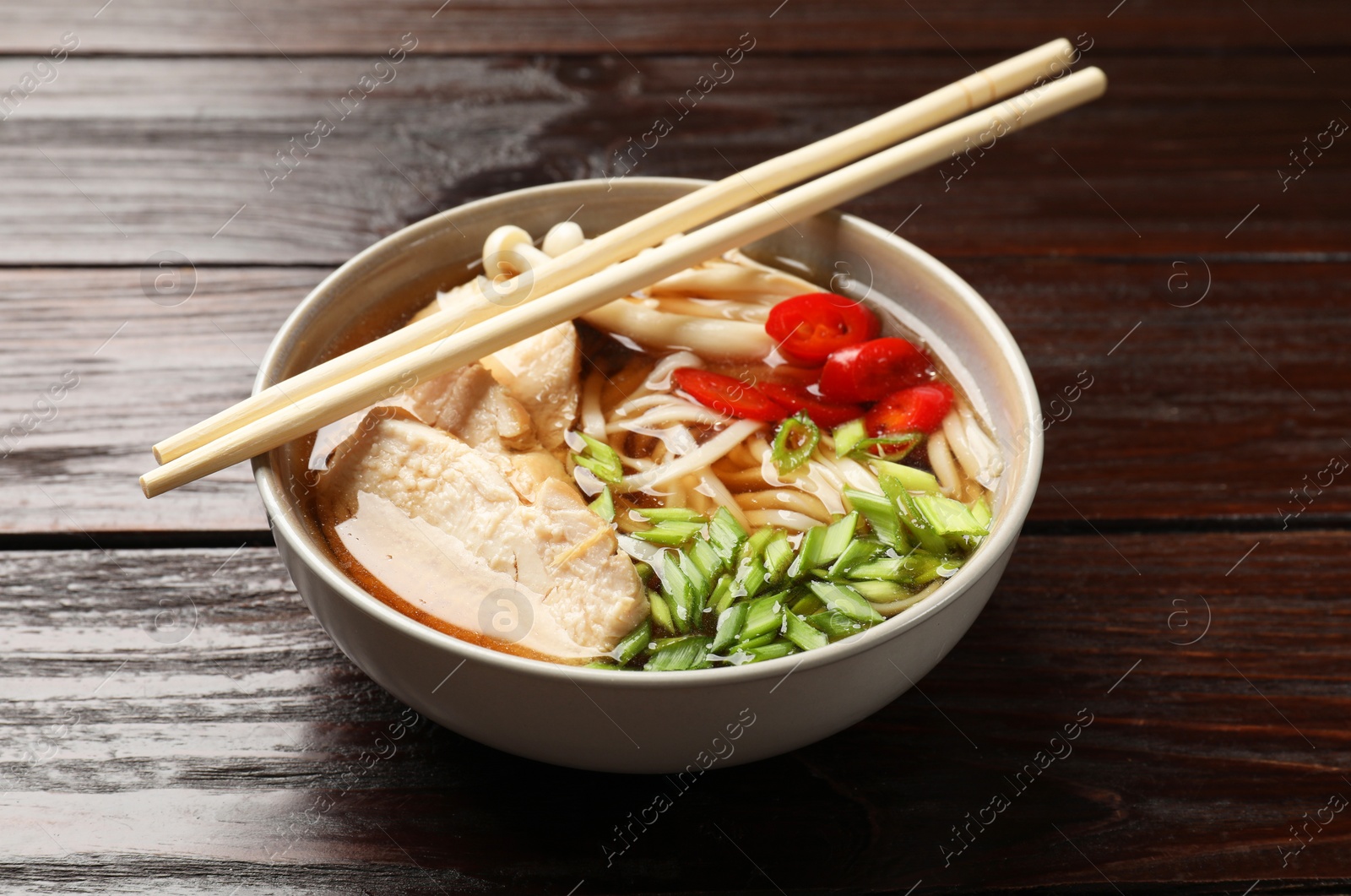 Photo of Delicious ramen with meat in bowl and chopsticks on wooden table. Noodle soup