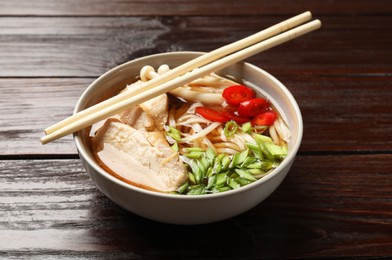 Photo of Delicious ramen with meat in bowl and chopsticks on wooden table. Noodle soup